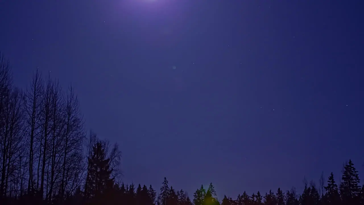 Time-lapse of the night sky and a full moon moving above a forest at night