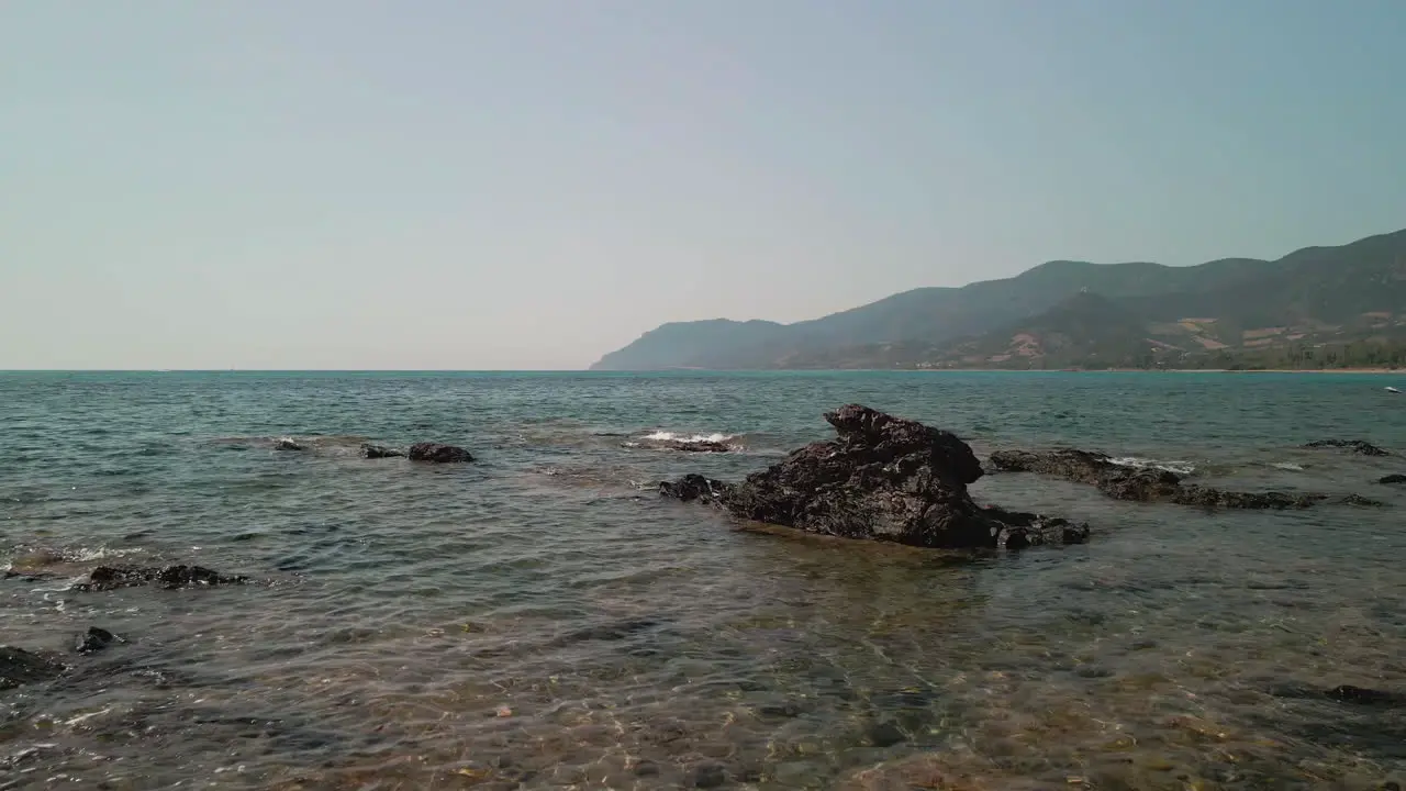 Sea Waves Crashing On The Rocks With Mountains In Background During The Summer Afternoon In Sardinia Italy aerial drone shot