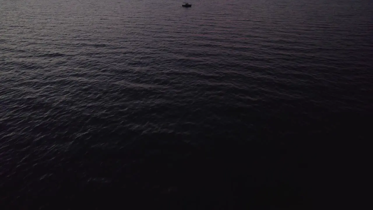 Small leisure boat floating in dark sea during nightfall aerial