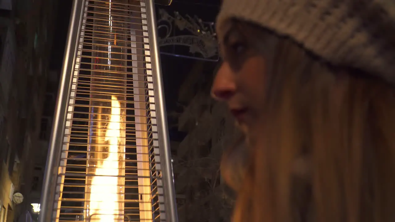 Woman with a hat placing her hair next to an outdoor stove that gives off a flame of fire and light