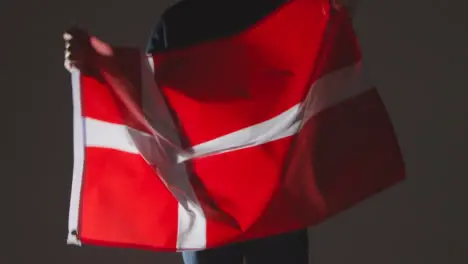 Studio Shot Of Anonymous Person Or Sports Fan Waving Flag Of Denmark Against Black Background