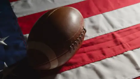 Low Key Lighting Studio Shot Of American Football Rolling Onto Stars And Stripes Flag