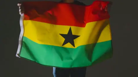 Studio Shot Of Anonymous Person Or Sports Fan Waving Flag Of Ghana Against Black Background