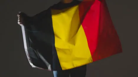 Studio Shot Of Anonymous Person Or Sports Fan Waving Flag Of Belgium Against Black Background