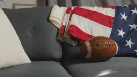 Lounge At Home Of Person Watching American Football Game On TV With Stars And Stripes Flag And Ball