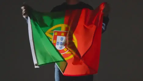 Studio Shot Of Anonymous Person Or Sports Fan Waving Flag Of Portugal Against Black Background