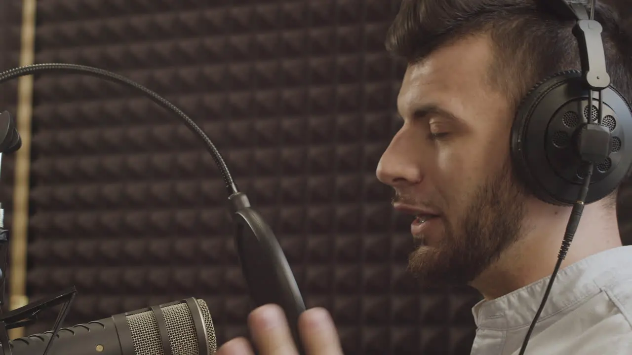 Primer Plano De Un Joven Presentador De Radio Con Barba Y Aparatos Ortopédicos Hablando Al Micrófono En Un Estudio De Grabación