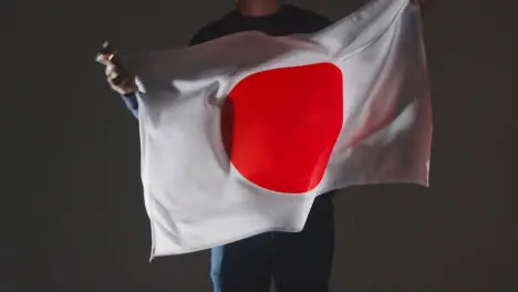 Studio Shot Of Anonymous Person Or Sports Fan Waving Flag Of Japan Against Black Background