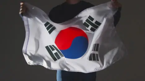 Studio Shot Of Anonymous Person Or Sports Fan Waving Flag Of South Korea Against Black Background