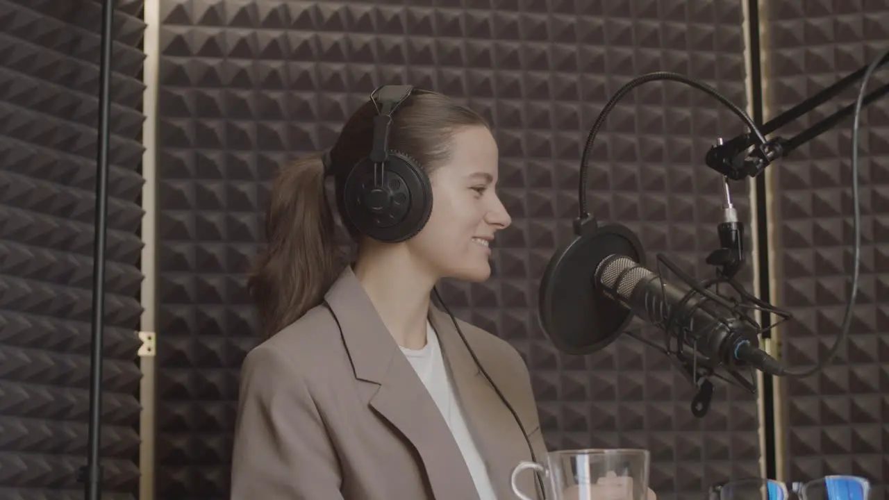 Eine Elegante Junge Frau Mit Zurückgebundenem Haar Und Lächelndem Anzug Hört Lächelnd Der Sprechenden Person In Einem Radioaufnahmestudio Zu