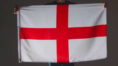 Studio Shot Of Anonymous Person Or Sports Fan Holding English Flag Of Saint George Against Black Background