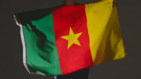 Studio Shot Of Anonymous Person Or Sports Fan Waving Flag Of Cameroon Against Black Background