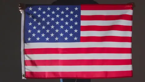 Studio Shot Of Anonymous Person Or Sports Fan Holding Flag Of America Against Black Background