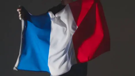 Studio Shot Of Anonymous Person Or Sports Fan Waving Flag Of France Against Black Background