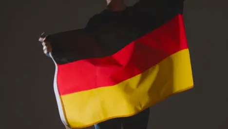 Studio Shot Of Anonymous Person Or Sports Fan Waving Flag Of Germany Against Black Background