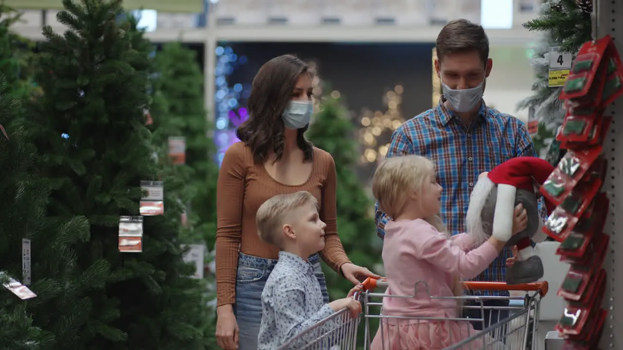 The family chooses the scenery in the supermarket A happy family in medical masks in the store buys Christmas decorations and gifts in slow motion