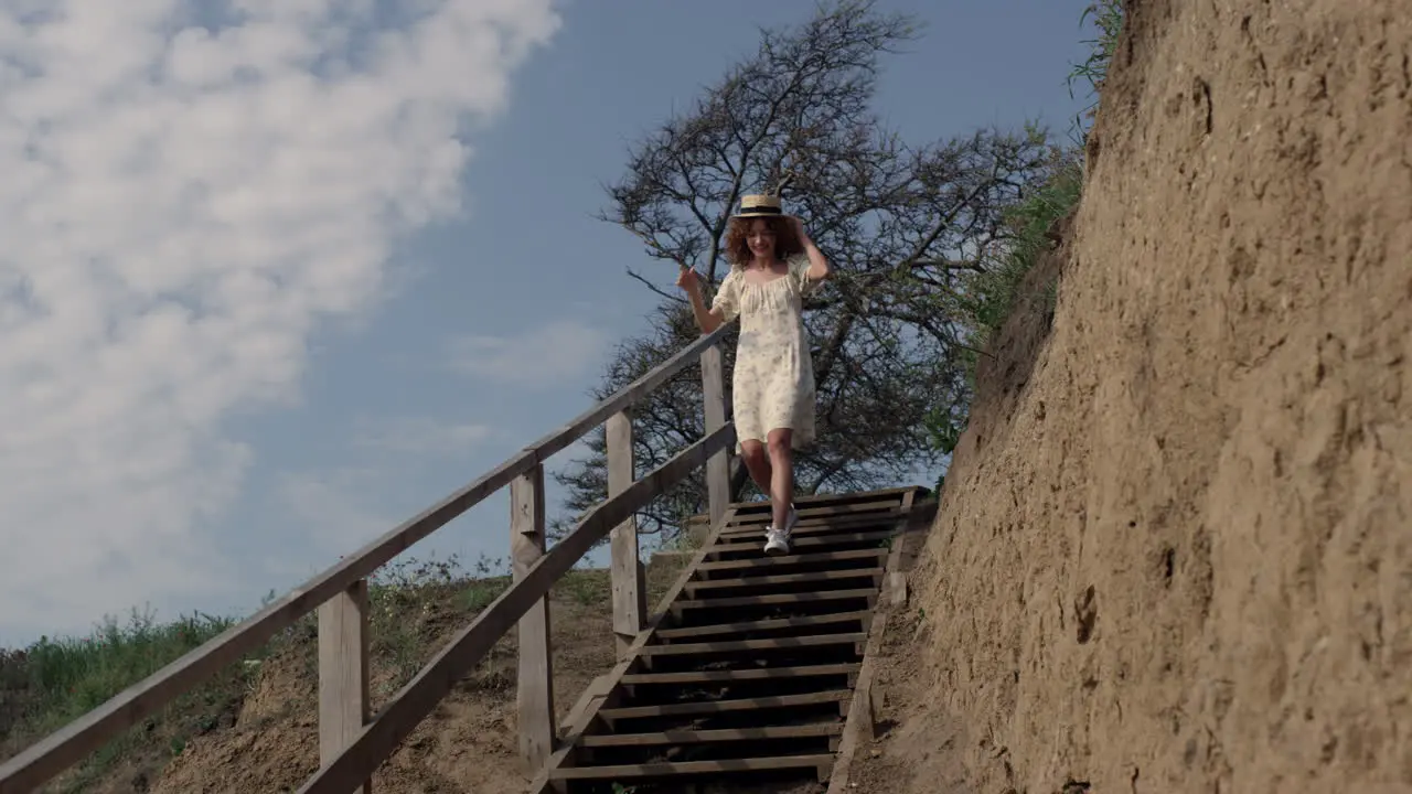 Energetic woman hurrying downstairs sand beach holding straw hat on head