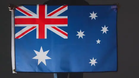 Studio Shot Of Anonymous Person Or Sports Fan Holding Flag Of Australia Against Black Background