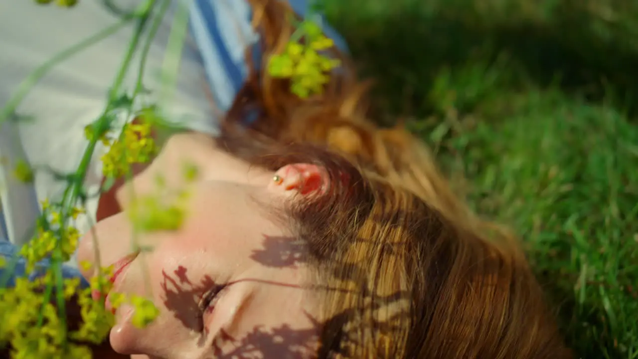 Relaxed redhar woman touching face with spring flower on green grass background