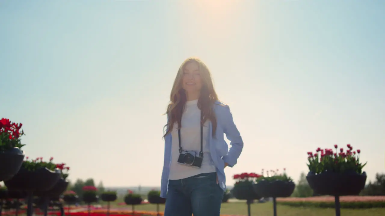 Smiling girl in jeans standing with camera in blossomed spring park in sunshine