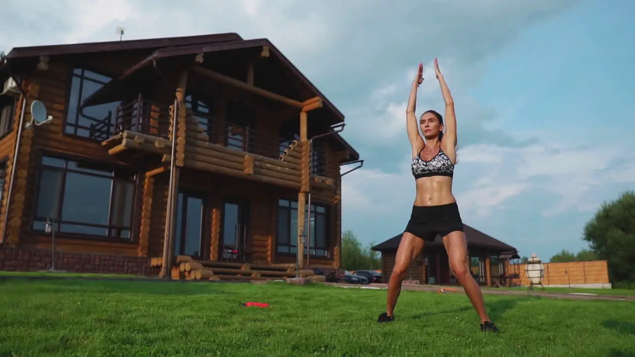 Slim beautiful woman in sportswear on the background of the house on the lawn performs jumps for cardio training and fat burning