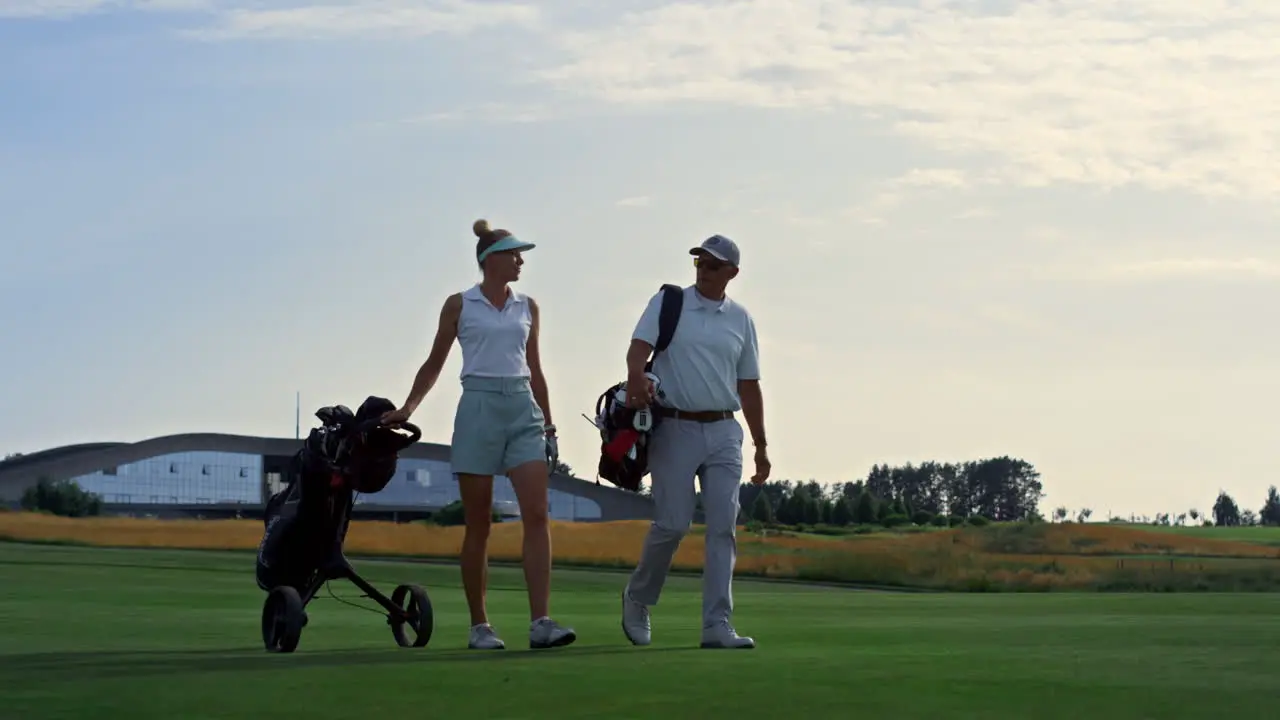 Couple golf players discuss sport course outside Two golfers walk grass field