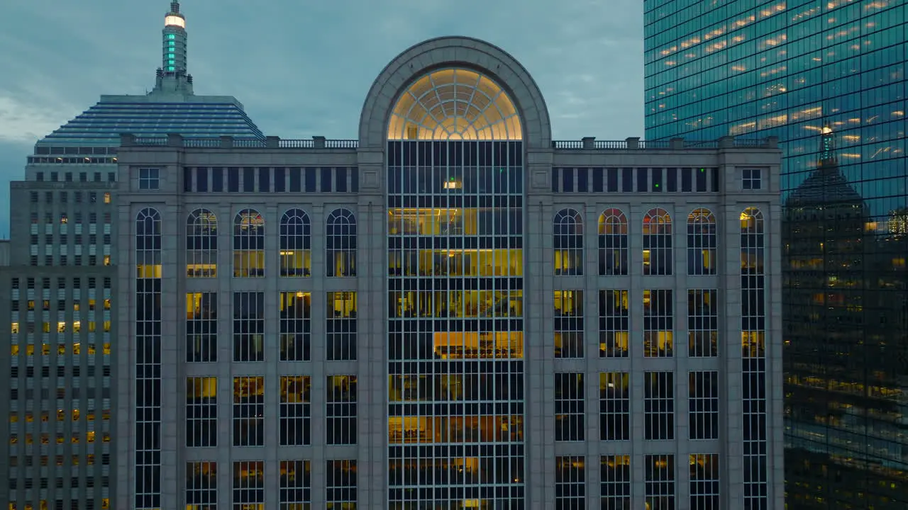 Pull back shot of illuminated interior of high rise commercial building at dusk Backwards reveal of surrounding downtown office buildings Boston USA