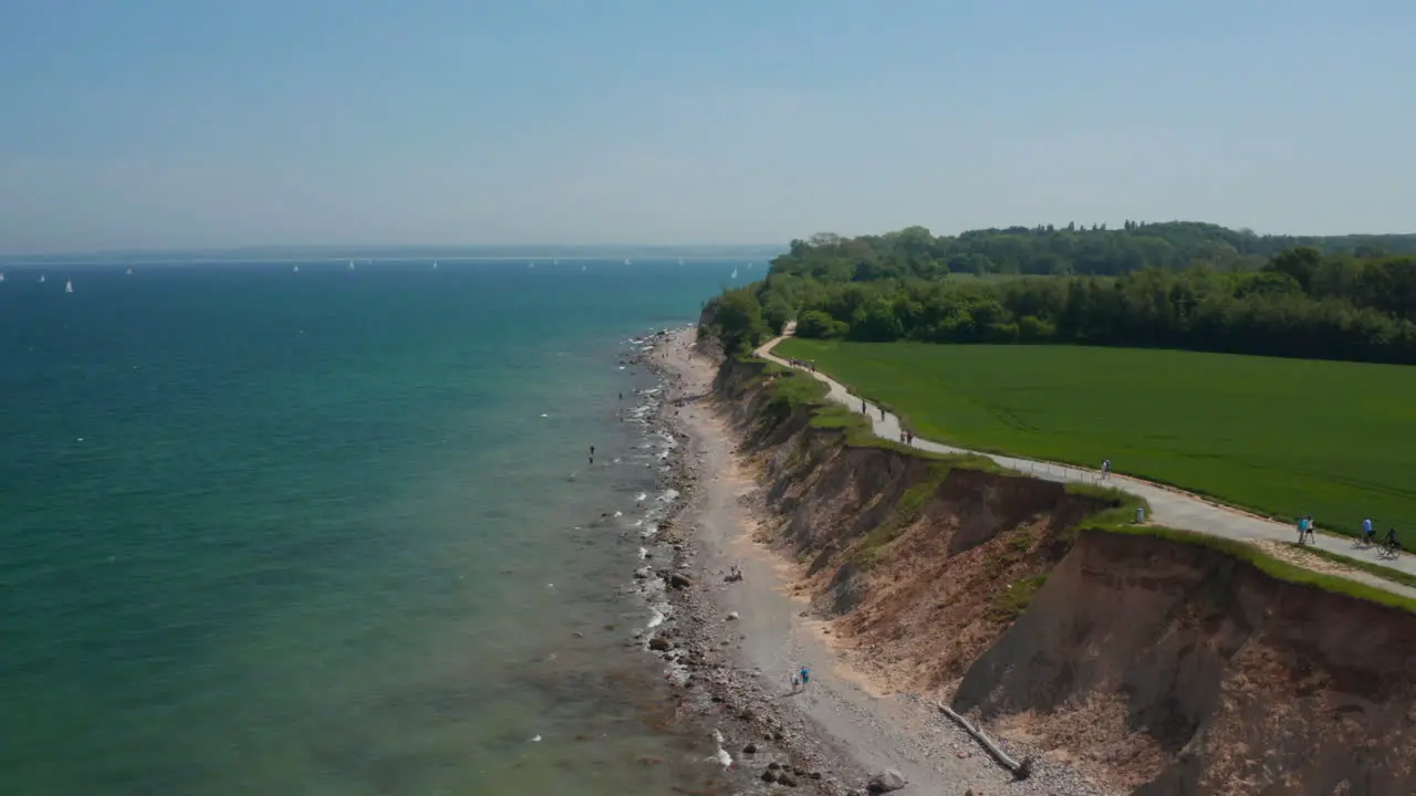 Aerial view of German coastline facing Baltic sea vast green field by coast with pathway people passing by clear sky day forward