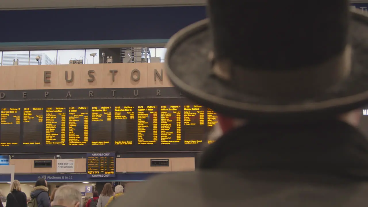 Man wearing hat looking at Euston Station departure board