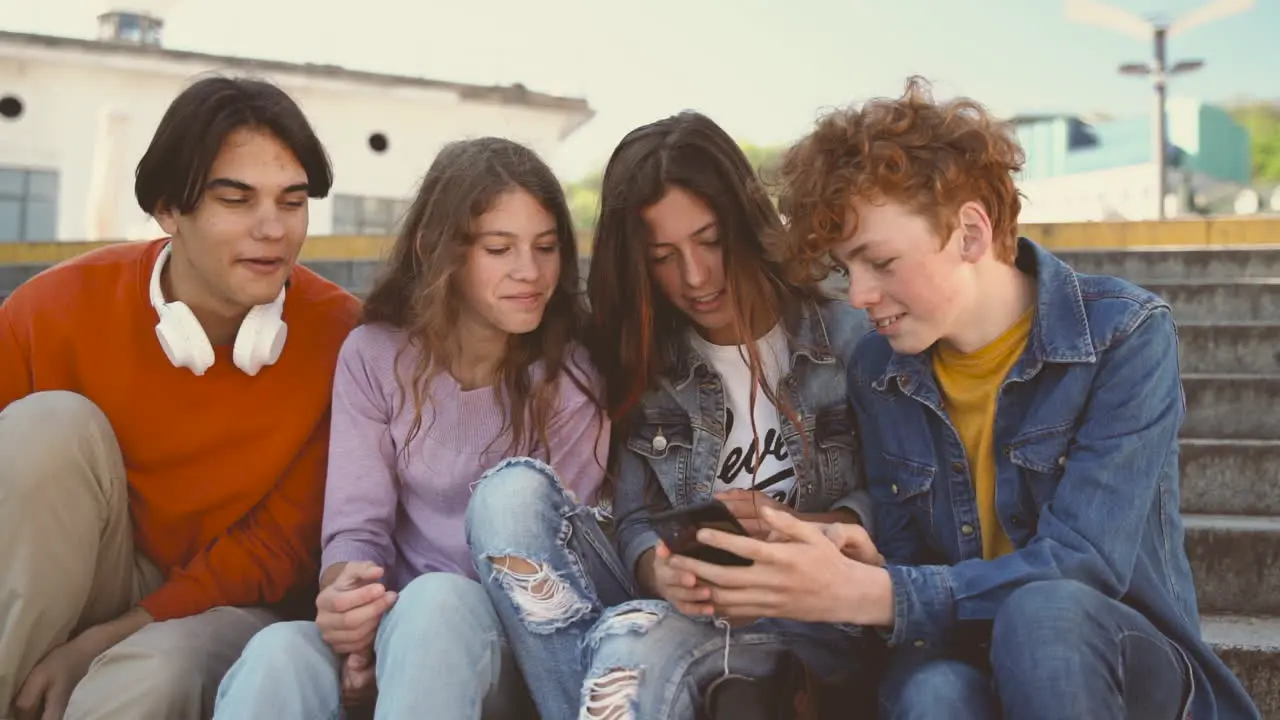 A Group Of Teenagers With Two Girls And Two Boys Watching Something Funny On A Cell Phone 1