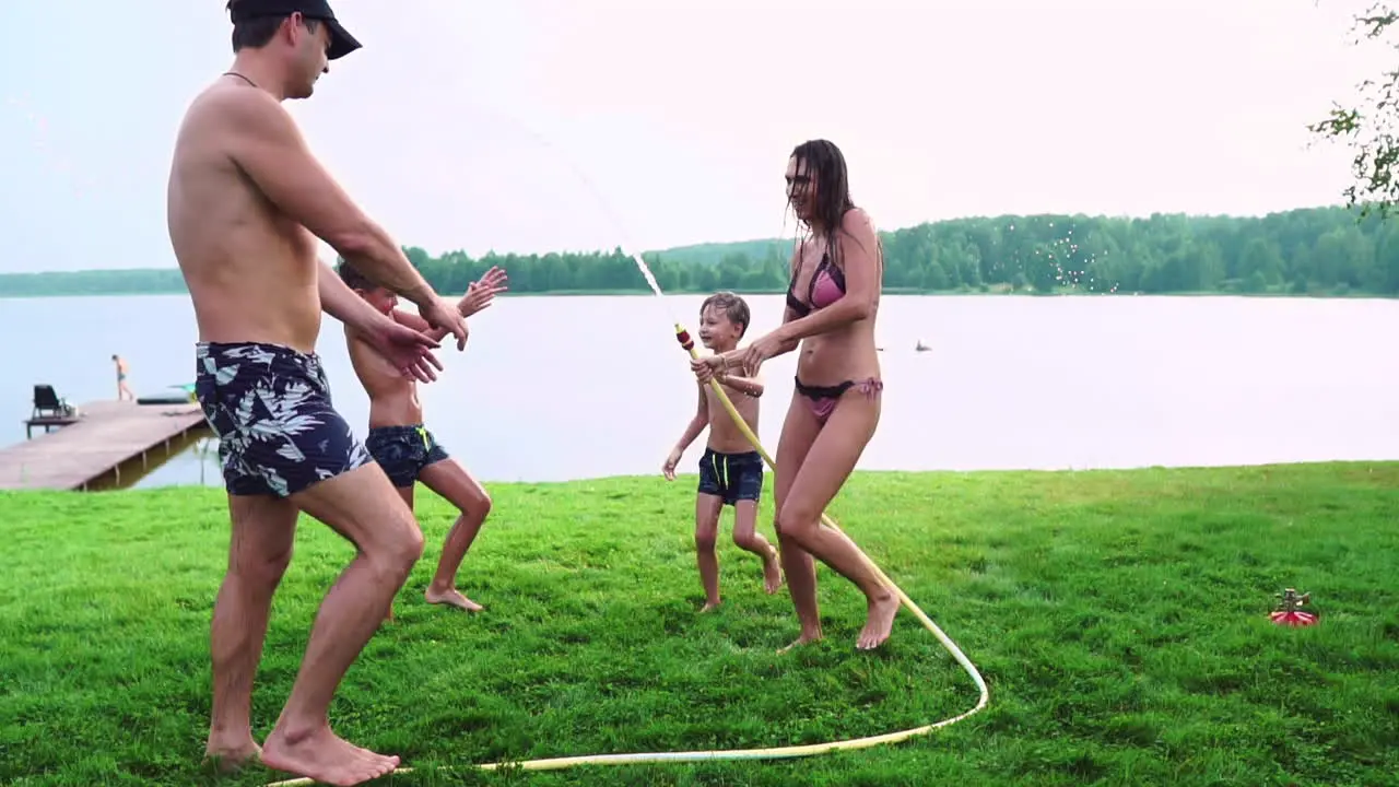 Mother with father and two children playing on the lawn pouring water laughing and having fun on the Playground with lawn on the background of his house near the lake in slow motion