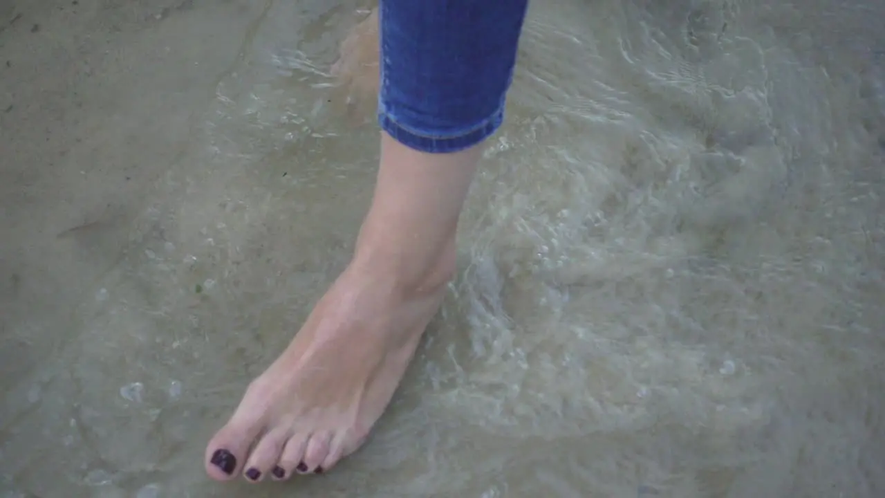 Female bare foot standing and moving sea water on background sandy bottom