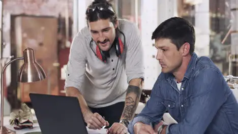 two young men using a laptop in a welding workshop