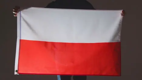 Studio Shot Of Anonymous Person Or Sports Fan Holding Flag Of Poland Against Black Background