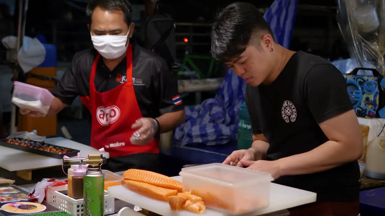 Two chefs preparing fish on street food stall night market Bangkok