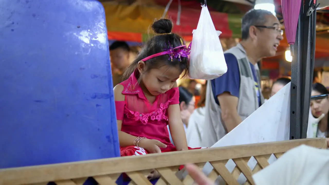 Young girl sitting playing bored on her phone busy night market Bangkok