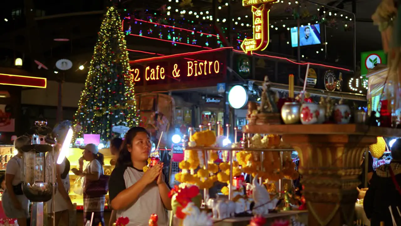 Praying Woman on Buddhist altar at Night market tourists passing by Bangkok