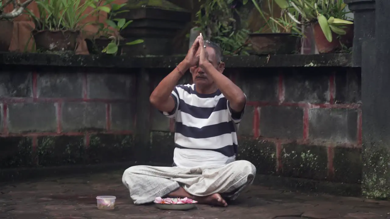 Portrait of Balinese male praying with hands at forehead Sitting outside of Hindu Temple