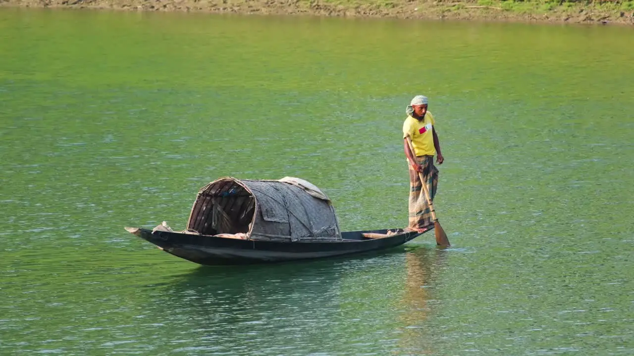 Asian fisherman stands on traditional wooden fishing boat surma river