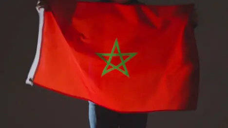 Studio Shot Of Anonymous Person Or Sports Fan Waving Flag Of Morocco Against Black Background