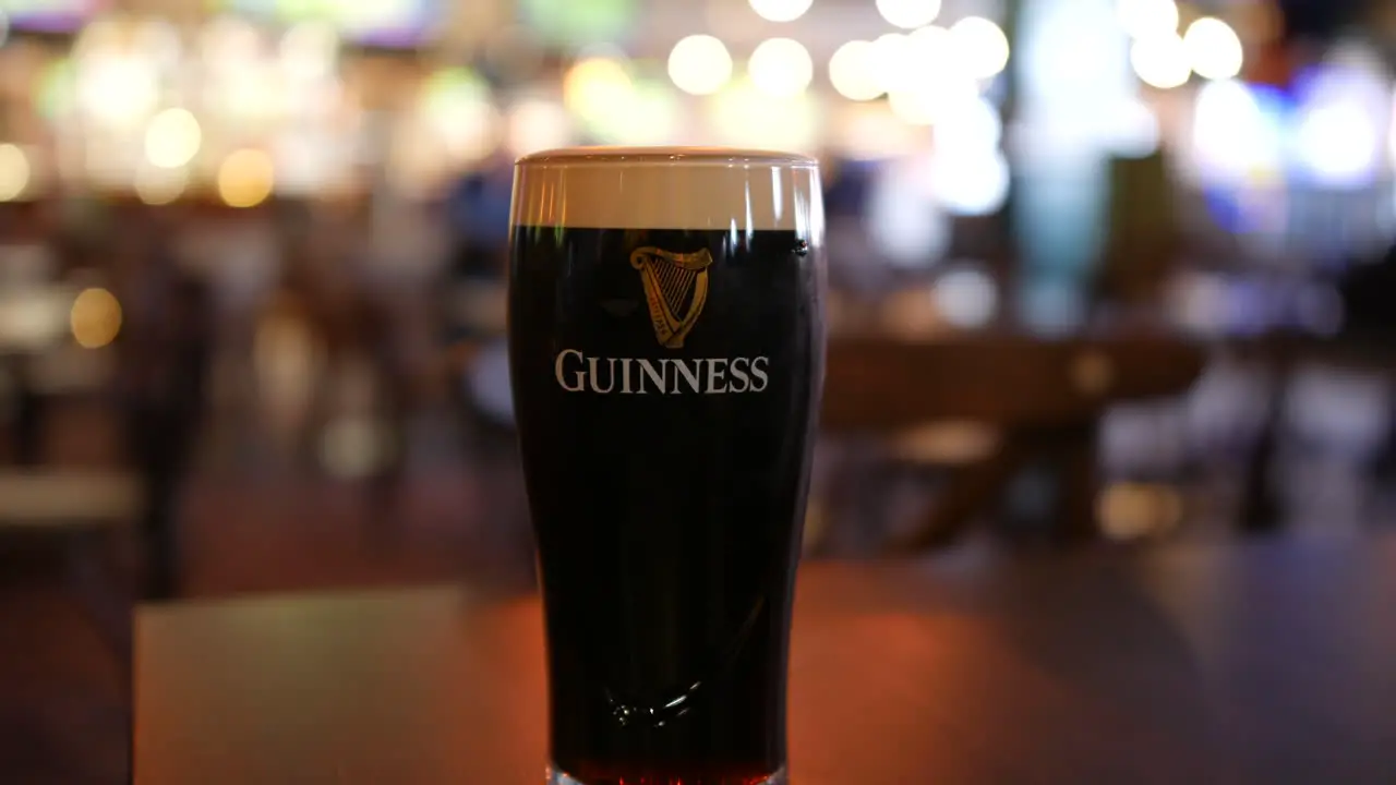 A pint of Guinness stout ale beer on a table in an Irish pub on St Patrick's day in Ireland with customers walking by