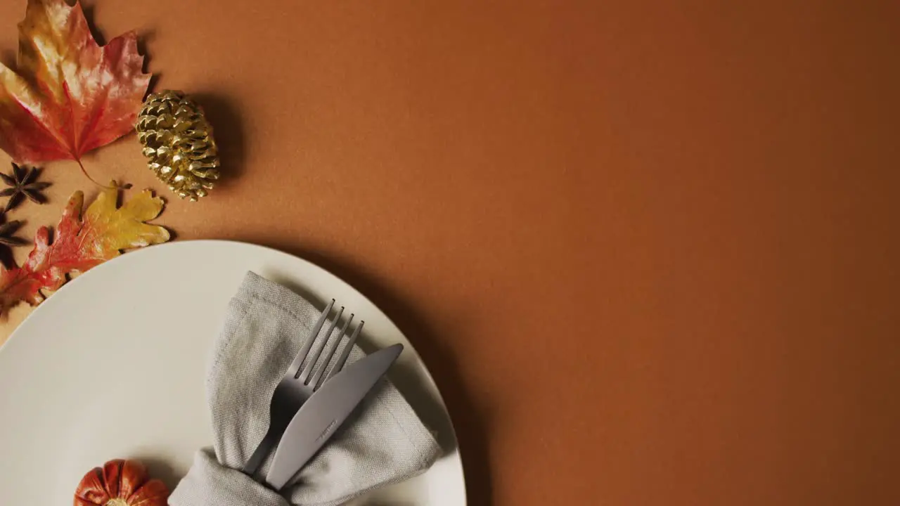 Video of plate with cutlery and autumn decoration with leaves on orange surface