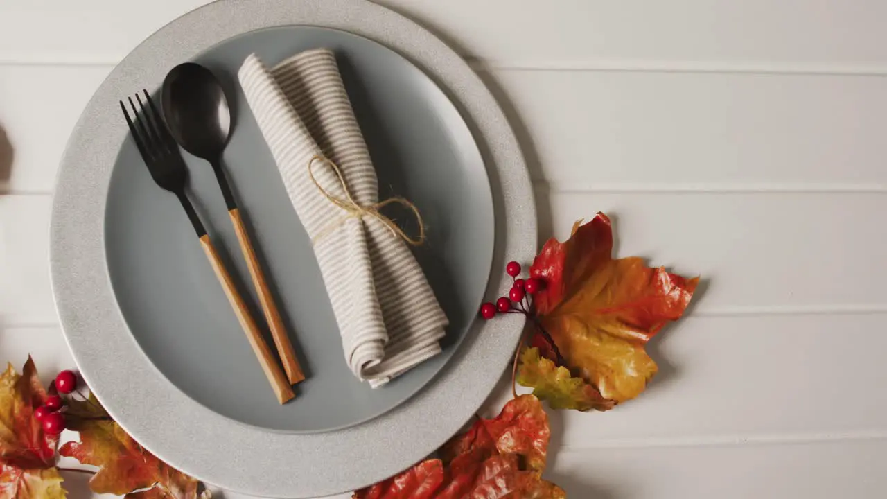 Video of plate with cutlery and autumn decoration with leaves on white surface