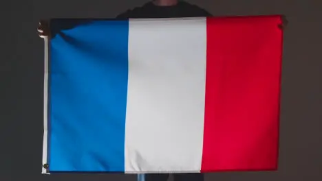 Studio Shot Of Anonymous Person Or Sports Fan Holding Flag Of France Against Black Background