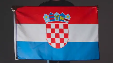 Studio Shot Of Anonymous Person Or Sports Fan Holding Flag Of Croatia Against Black Background