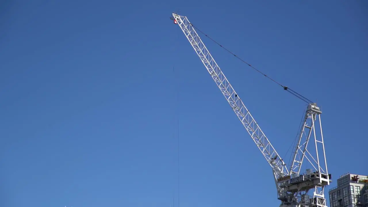 White construction crane stands tall above city skyline against blue skies