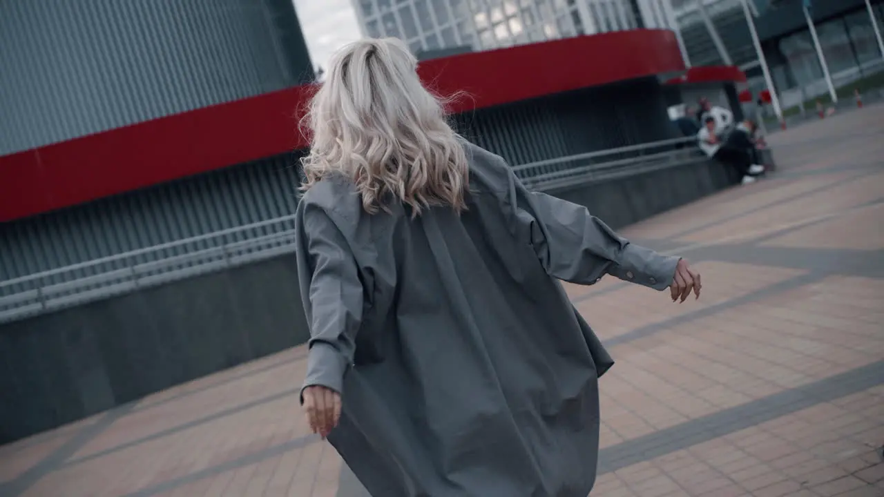 Excited girl walking downtown touching hair near urban city buildings