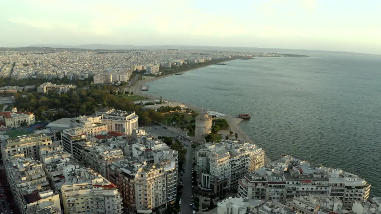 cinematic smooth aerial drone shot looking out to sea with the city of Thessaloniki in view at sunset with the white tower of Thessaloniki in the middle Greece in 4k