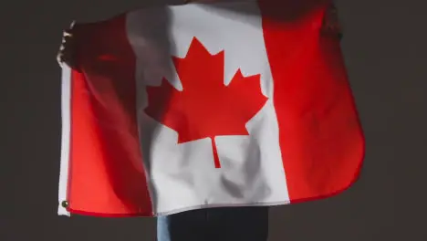 Studio Shot Of Anonymous Person Or Sports Fan Waving Flag Of Canada Against Black Background