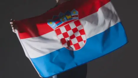 Studio Shot Of Anonymous Person Or Sports Fan Waving Flag Of Croatia Against Black Background